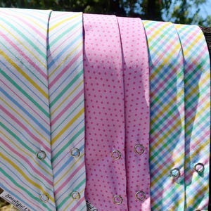 May include: A collection of fabric bandanas featuring various patterns including pastel diagonal stripes, pink polka dots, and a multi-coloured gingham check. Each bandana is secured with silver metal snaps and includes a tag labelled Beautiful Chaos.