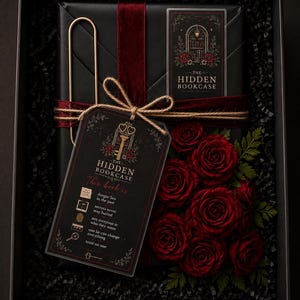 Op de afbeelding: Een zwarte geschenkdoos met een boek verpakt in zwart papier met een donkerrood fluwelen lint, een gouden paperclip en een label met de tekst The Hidden Bookcase. Het label bevat zinnen zoals danger lies in the past en rode rozen.
