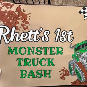 May include: A tan banner with the text "Rhett's 1st MONSTER TRUCK BASH" in white and green. A green monster truck illustration is shown on a brown mound, with a checkered flag banner in the upper right corner.