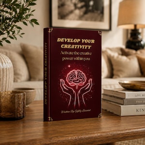 Peut inclure: Un livre marron intitulé "DEVELOP YOUR CREATIVITY" avec une illustration de cerveau. Le livre est sur une table en bois avec d'autres objets décoratifs, dont un vase avec de la verdure, un verre et des livres empilés.