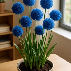 Puede incluir: Un arreglo en maceta de flores de allium azules artificiales. Las cabezas de las flores esféricas son de un azul vibrante, contrastando con los tallos y hojas verdes. La maceta es de color gris claro y el arreglo está sobre una superficie de madera.