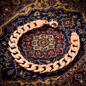 Pode incluir: Uma pulseira de corrente tipo grumet em tom de ouro rosa com elos grossos, polidos e entrelaçados. A pulseira é fixada com um fecho lagosta em uma das extremidades, exibindo um design arredondado e contínuo em toda a peça.