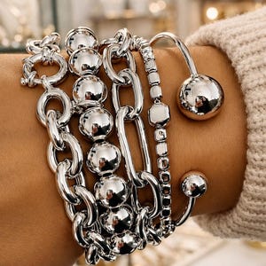 May include: Several silver bracelets of different styles. The bracelets feature chain links, beaded strands, and a cuff with a sphere detail. The word "BARVEDA" is visible in the background.