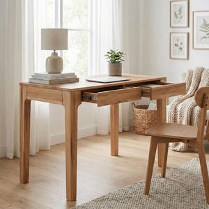 Peut inclure: Un bureau en bois clair avec deux tiroirs ouverts, une chaise assortie et une petite plante en pot. Une lampe beige est posée sur le bureau, ainsi que des livres et un ordinateur portable. Le bureau est placé devant une fenêtre avec des rideaux transparents.