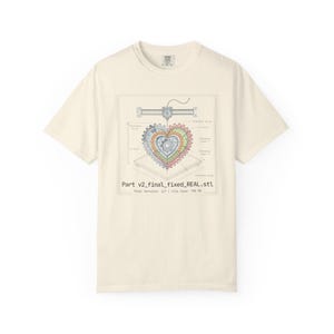 Può includere: T-shirt color crema con un diagramma dettagliato di un design a ingranaggi a forma di cuore, con la scritta "Part v2_final_fixed_REAL.stl". Il design include un'illustrazione di una stampante 3D e annotazioni tecniche. Un capo casual.