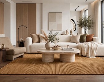 May include: A living room featuring a cream-colored sectional sofa with beige, olive, and rust-colored pillows, a low oval travertine coffee table, a textured amber-colored area rug, a beige armchair, and a dark wood side table.