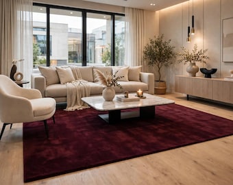 May include: A large, rectangular, deep burgundy area rug with a soft, plush texture, positioned in a living room beneath a white marble coffee table, a beige sofa, and a matching armchair, covering a light-colored wooden floor.