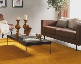 May include: A rectangular black coffee table with thin metal legs, topped with two tall mustard yellow candle holders, white pillar candles, a small abstract wooden head sculpture, a small bowl, and stacked books, set on a large mustard yellow rug.