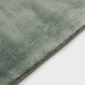 May include: A sage green rug with a soft, dense, and short-pile texture. The rectangular textile features a clean, finished edge and a uniform, solid color surface that displays subtle variations in light and shadow across the fibers.