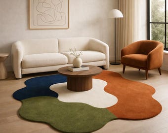 May include: A modern living room featuring a multi-colored area rug with an abstract design. The rug has sections of navy blue, olive green, white, and rust orange. A cream-colored sofa, a wooden coffee table, and an orange armchair complete the scene.