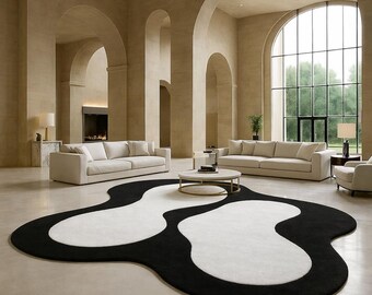 May include: A modern living room featuring a large black and white abstract rug. The rug's design contrasts with the neutral tones of the sofas, walls, and arched doorways. The room is filled with natural light from a large window.