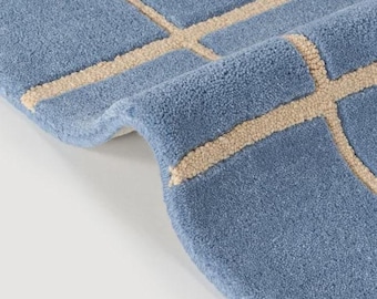 May include: A blue area rug featuring a grid pattern of raised, beige-colored lines. The rug has a thick, tufted texture with a soft pile, and one corner is folded over to reveal the depth and construction of the material.