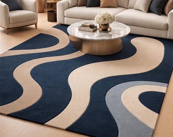 May include: A large, modern area rug with a navy blue background and flowing, wave-like patterns in beige and light gray. The rug is placed in a living room setting with a sofa, armchair, and coffee table.