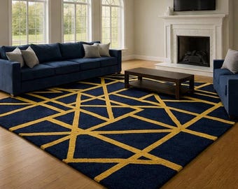 May include: A navy blue area rug with a geometric gold pattern. The rug is placed in a living room with navy blue sofas, a dark brown coffee table, and a fireplace. The room has large arched windows.
