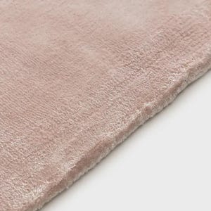 May include: A soft, plush rug in a muted dusty rose color. The surface features a dense, short-pile texture that creates subtle variations in light and shadow across the fabric. The edge of the rug is finished with a clean, straight hem.