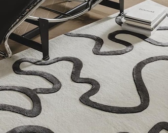 May include: A rectangular area rug featuring a cream-colored base with a raised, dark gray, continuous wavy line pattern that creates organic, interconnected shapes across the surface. The rug has a soft, textured pile and a distinct tufted design.