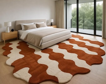 May include: A modern bedroom features a large, wavy-patterned rug in shades of rust and cream. The rug sits on a wooden floor, complementing the neutral tones of the bed and surrounding furniture. The room has large windows and natural light.