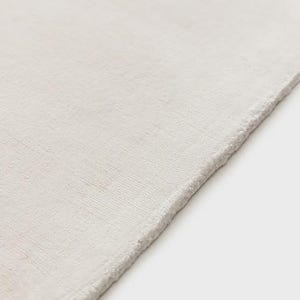 May include: A solid off-white rug with a dense, short-pile texture and a clean, straight edge. The surface features a subtle, uniform weave pattern that covers the entire visible area, creating a consistent and neutral appearance throughout.