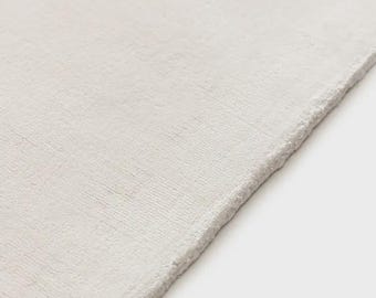 May include: A solid off-white rug with a dense, short-pile texture and a clean, straight edge. The surface features a subtle, uniform weave pattern that covers the entire visible area, creating a consistent and neutral appearance throughout.