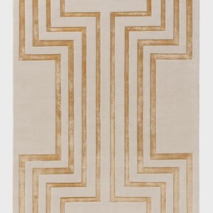 May include: A rectangular area rug featuring a cream-colored base with a symmetrical, raised geometric pattern in a golden-tan hue. The design consists of vertical and zigzagging lines that create a structured, maze-like motif across the surface.