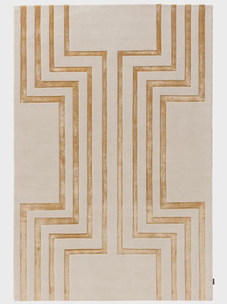 May include: A rectangular area rug featuring a cream-colored base with a symmetrical, raised geometric pattern in a golden-tan hue. The design consists of vertical and zigzagging lines that create a structured, maze-like motif across the surface.
