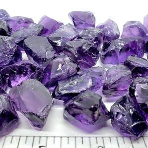 Puede incluir: Un conjunto de cristales de amatista en bruto, sin cortar. Los cristales, de tamaños y formas variadas, presentan un color púrpura intenso con zonas translúcidas. Se aprecia la textura rugosa y las formas naturales de las piedras.