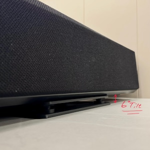 Op de afbeelding: Een zwarte soundbar gemonteerd op een zwarte kunststof standaard die een kanteling van 6 graden biedt. De soundbar is voorzien van een zwarte, textuurrijke stoffen grille aan de voorzijde. De standaard is laag en rechthoekig onder het apparaat.
