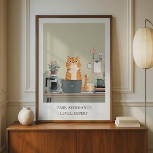 Könnte beinhalten: Gerahmter Druck mit einer orangefarbenen Tabby-Katze, die an einem Laptop arbeitet. Der Text "TASK AVOIDANCE LEVEL: EXPERT" ist darunter zu sehen. Das Bild befindet sich in einem Raum mit einer Lampe und einem Holzschrank.