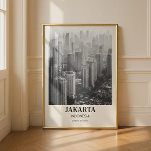 May include: A framed black and white photograph of Jakarta, Indonesia, showing a cityscape of tall buildings. The photograph is in a gold frame and includes the city's name and coordinates at the bottom.