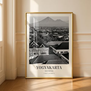 Op de afbeelding: Een zwart-wit ingelijste wandkunstprint met een landschap van Yogyakarta, Indonesië, met een berg op de achtergrond. De tekst luidt YOGYAKARTA, INDONESIA, en de coördinaten 7.7956 S, 110.3695 E in een strak, zwart schreeflettertype.