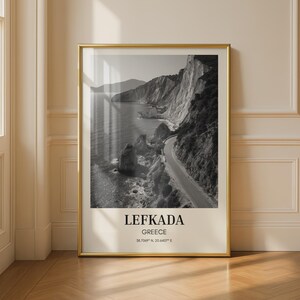 Könnte beinhalten: Schwarz-Weiß-Druck von Lefkada, Griechenland, in einem Rahmen. Das Bild zeigt eine Küstenstraße entlang einer Klippe, mit dem Meer auf der linken Seite. Der Druck hat einen goldenen Rahmen und den Text "LEFKADA GREECE" am unteren Rand.