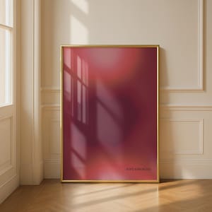 Peut inclure: Une affiche encadrée avec un cadre doré. L'œuvre présente un dégradé flou de teintes rouges et bordeaux. Le texte "SOFT STRENGTH" est imprimé en bas à droite. L'affiche est appuyée contre un mur avec une fenêtre et une porte.