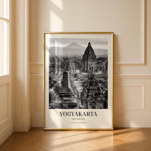 May include: A framed black and white wall art print featuring the Prambanan temple complex in Yogyakarta, Indonesia. The text reads YOGYAKARTA, INDONESIA, and the coordinates 7.7956 S, 110.5695 E. The print is encased in a thin gold metal frame.