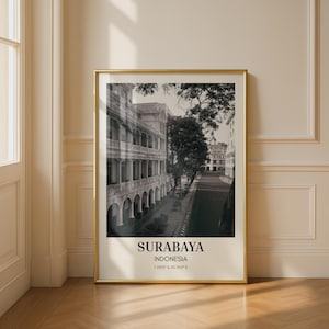 Può includere: Una stampa artistica da parete incorniciata verticale con una fotografia in bianco e nero di un edificio in stile coloniale con portici ad archi a Surabaya, in Indonesia. Il testo SURABAYA, INDONESIA e le coordinate 7.2575° S, 112.7521° E appaiono sotto.