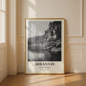 Könnte beinhalten: Gerahmte Schwarz-Weiß-Fotografie einer Flussszene in Arkansas, USA. Das Bild zeigt einen Fluss, der durch eine felsige Landschaft mit Bäumen auf den Klippen fließt. Der Text "ARKANSAS UNITED STATES" befindet sich unten.