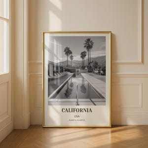 Könnte beinhalten: Schwarz-Weiß-Druck mit Rahmen, der eine Poolszene mit Palmen und Bergen zeigt. Der Druck enthält den Text "CALIFORNIA USA" und Koordinaten. Der Rahmen ist goldfarben.