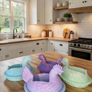 Puede incluir: Una colecci&oacute;n de coloridos portahuevos con forma de gallina en una cocina. Los soportes son en tonos de azul, morado y verde, con dise&ntilde;os detallados de plumas y nidos. Se colocan sobre una encimera de madera.