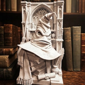 May include: A light gray, textured 3D-printed sculpture featuring a weathered, folded wizard hat resting atop a stack of books. The scene includes a scarf, a quill in an inkwell, a scroll, and a wand, all set against a detailed gothic archway.