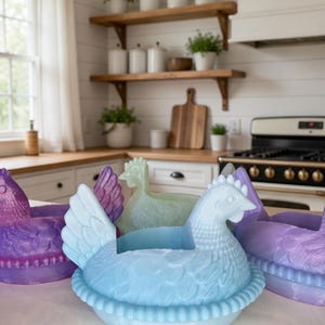 Puede incluir: Una colecci&oacute;n de recipientes con forma de gallina en tonos azul, morado y verde. Los recipientes est&aacute;n dise&ntilde;ados con detalles de plumas y nidos, perfectos para la decoraci&oacute;n de la cocina o exhibiciones de Pascua.