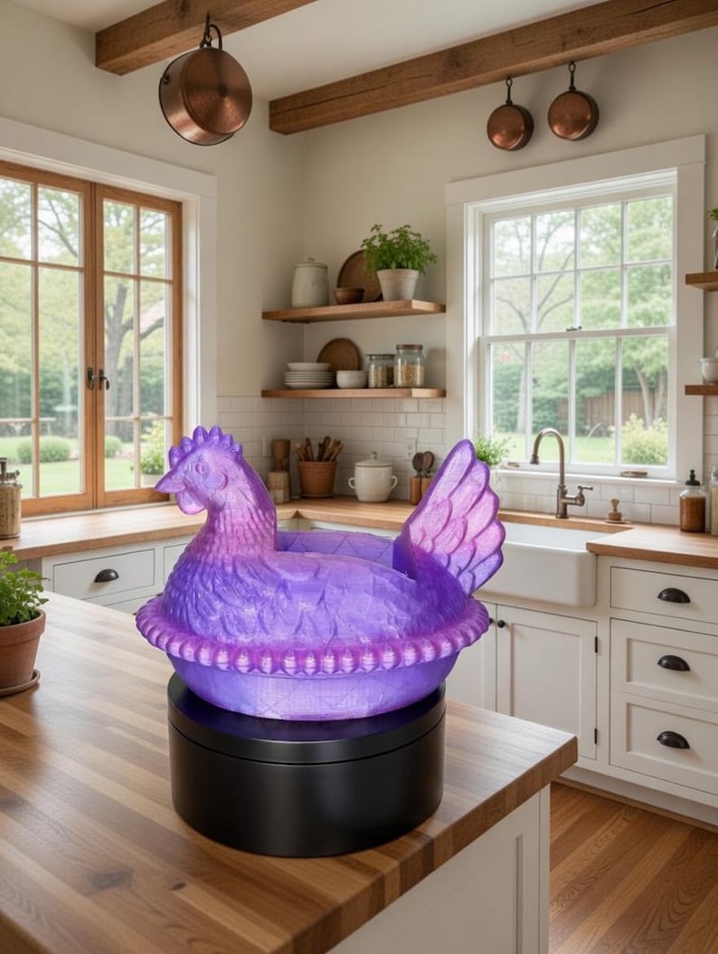 Puede incluir: Un plato decorativo en forma de pollo morado y rosa sobre una base giratoria negra. El plato est&aacute; hecho de un material texturizado y est&aacute; colocado sobre una encimera de madera en un entorno de cocina. La cocina tiene gabinetes blancos y vigas de madera.