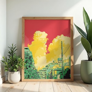 Peut inclure: Une affiche encadrée représente un paysage urbain avec un ciel rouge et des nuages jaunes. Les bâtiments sont rendus dans des tons de vert et de jaune. L'affiche est dans un cadre en bois clair et est exposée avec des plantes en pot.