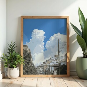 Peut inclure: Une impression d'art encadrée représentant une scène de rue avec des bâtiments, des lignes électriques et un ciel bleu vif rempli de nuages blancs et duveteux. L'œuvre est dans un cadre en bois et est exposée sur un sol en bois avec des plantes en pot de chaque côté.
