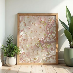 以下が含まれることがあります： ピンクと白の花が咲く桜の繊細な枝のクローズアップが特徴の額入りプリント。木製のフレームは、明るい木製の床に展示された花の芸術作品を引き立てます。