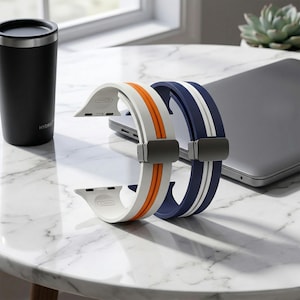 May include: Two silicone watch bands, one white with an orange stripe and the other navy blue with a white stripe. Both bands are 42mm and have a gray clasp. A black Hydro Flask and a laptop are in the background.