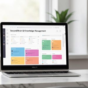 May include: A silver laptop displaying a webpage titled "Second Brain & Knowledge Management." The screen shows a dashboard with colorful blocks and icons. The laptop is on a white marble surface near a window.