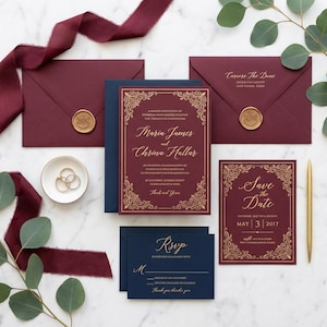 May include: A stylish wedding stationery set in burgundy and navy. The set includes invitations, RSVP cards, and save-the-date cards with gold decorative borders. Gold wax seals adorn the envelopes. A gold pen and wedding rings are also present.