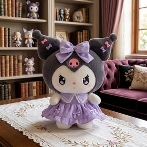 Könnte beinhalten: Eine Plüschpuppe mit grauem Kopf, großen Ohren und einer lila Schleife. Die Puppe trägt ein lila Kleid mit weißem Kragen und Schleifen. Die Puppe steht auf einem Tisch mit einer floralen Tischdecke.