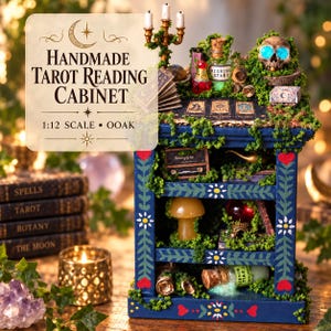 May include: A 1:12 scale handmade tarot reading cabinet featuring a blue frame with painted floral and heart motifs. The shelves contain miniature items including a skull, potion bottles, books, a mushroom, and a lamp, all adorned with green moss.
