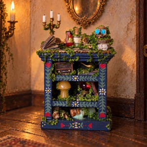 May include: A miniature dark blue wooden shelf unit decorated with painted flowers and red hearts, covered in green moss. The shelves hold tiny items including a skull with blue eyes, a mushroom, glass bottles, a radio, and a candelabra on top.