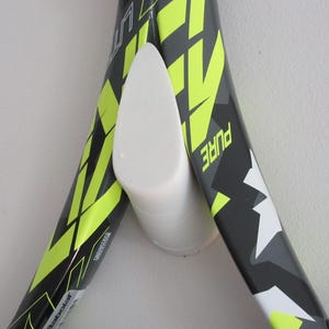 May include: A white tennis racket holder with two tennis rackets. The rackets are black and gray with neon yellow accents. The word "PURE" is visible on one racket.